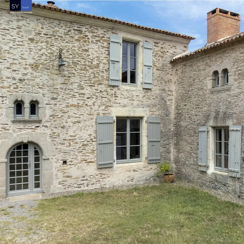 Maison en pierre rénovée avec fenêtres blanches et volets bleus